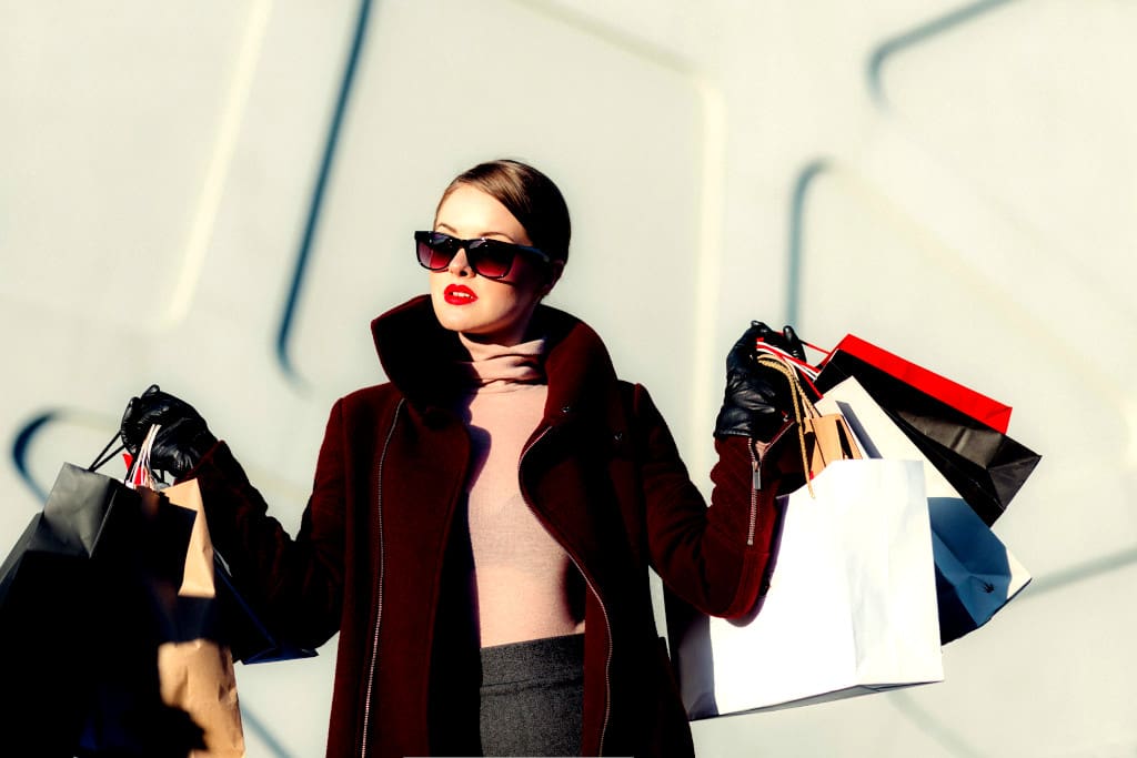 An elegant woman wearing sunglasses and holding shopping bags in both hands